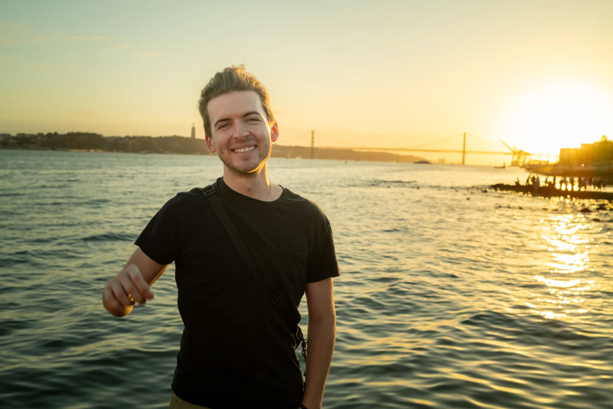 Dylan smiling by the water at sunset in Lisbon